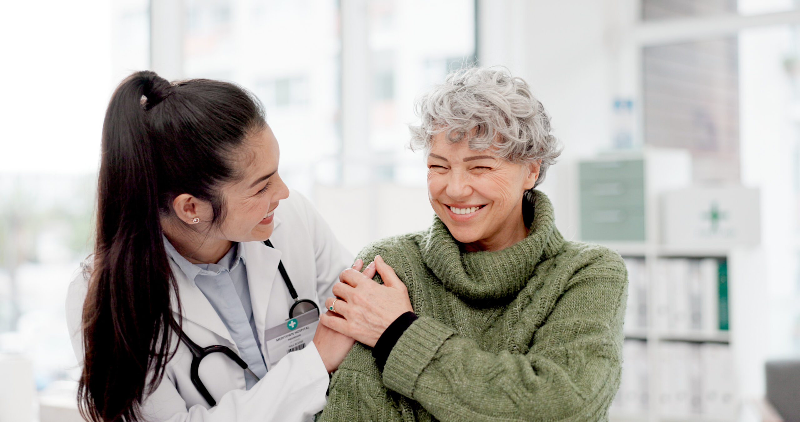 Happy, care and face of a doctor with a woman for medical trust, healthcare and help. Laughing, hug and portrait of a young nurse with a senior patient and love during a consultation at a clinic.